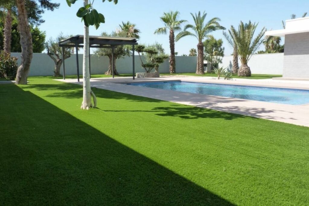 Jardín con césped artificial instalado por Flor & Design junto a una piscina
